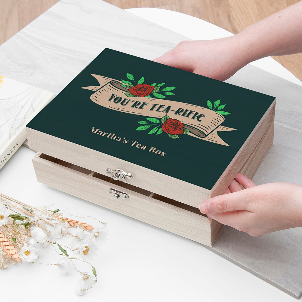 Tea box with decorative lid and text, held by a hand on a light surface.