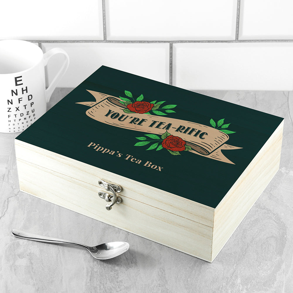 Wooden tea box with decorative lid featuring roses and text, placed on a tiled surface.