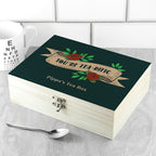 Wooden tea box with decorative lid featuring roses and text, placed on a tiled surface.