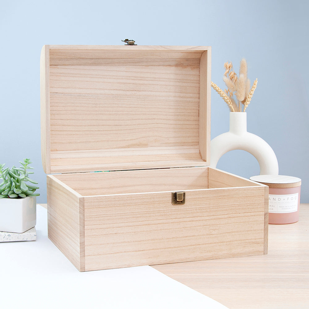 Wooden jewelry box on a light surface with a plant and candle in the background