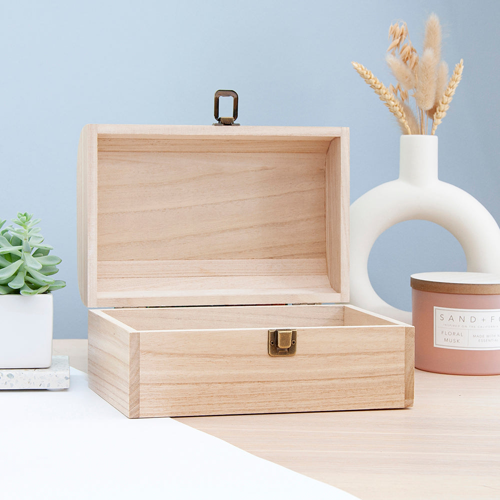 Wooden jewelry box on a table with decorative items including a vase with dried flowers and a candle.
