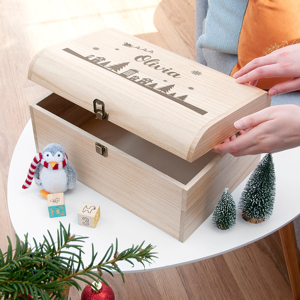 Wooden gift box with 'Olivia' engraved, surrounded by Christmas decorations on a table.