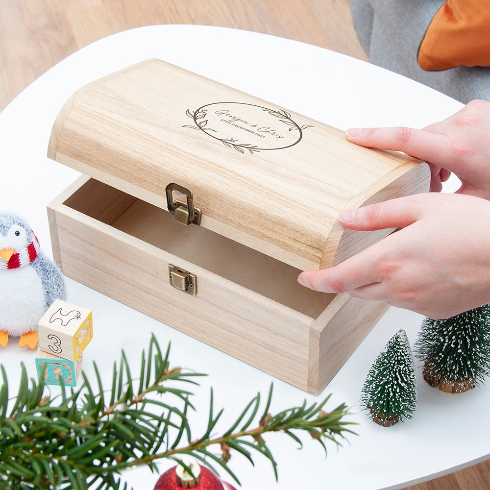 Wooden jewelry box with a hand opening it, surrounded by Christmas decorations.