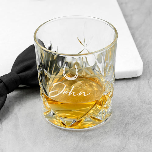 Clear glass with engraved name filled with a yellow liquid on a gray surface.