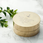 Round brass box with engraved text on a marble surface with green leaves.