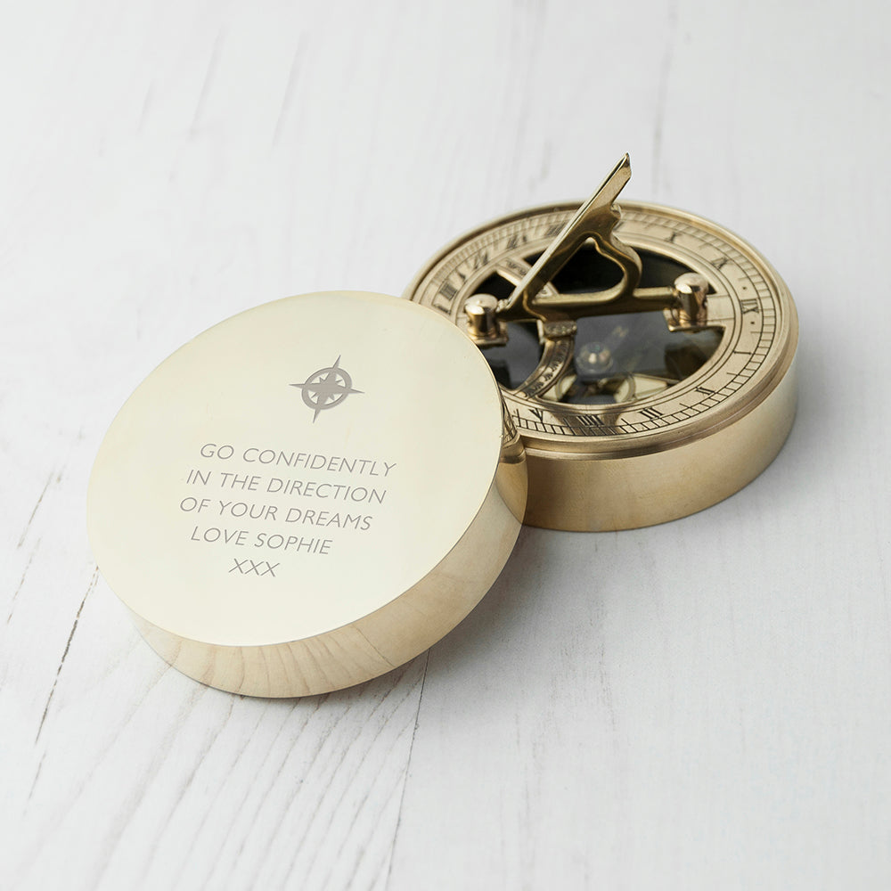 Brass compass with engraved message on a white wooden surface