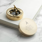 Gold compass with engraved message on a marble surface