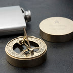 Brass compass and silver flask on a dark surface
