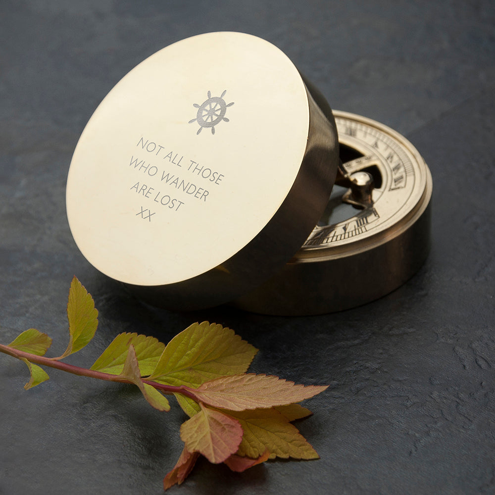Brass compass with engraved text on a dark surface with leaves