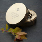 Brass compass with engraved text on a dark surface with leaves