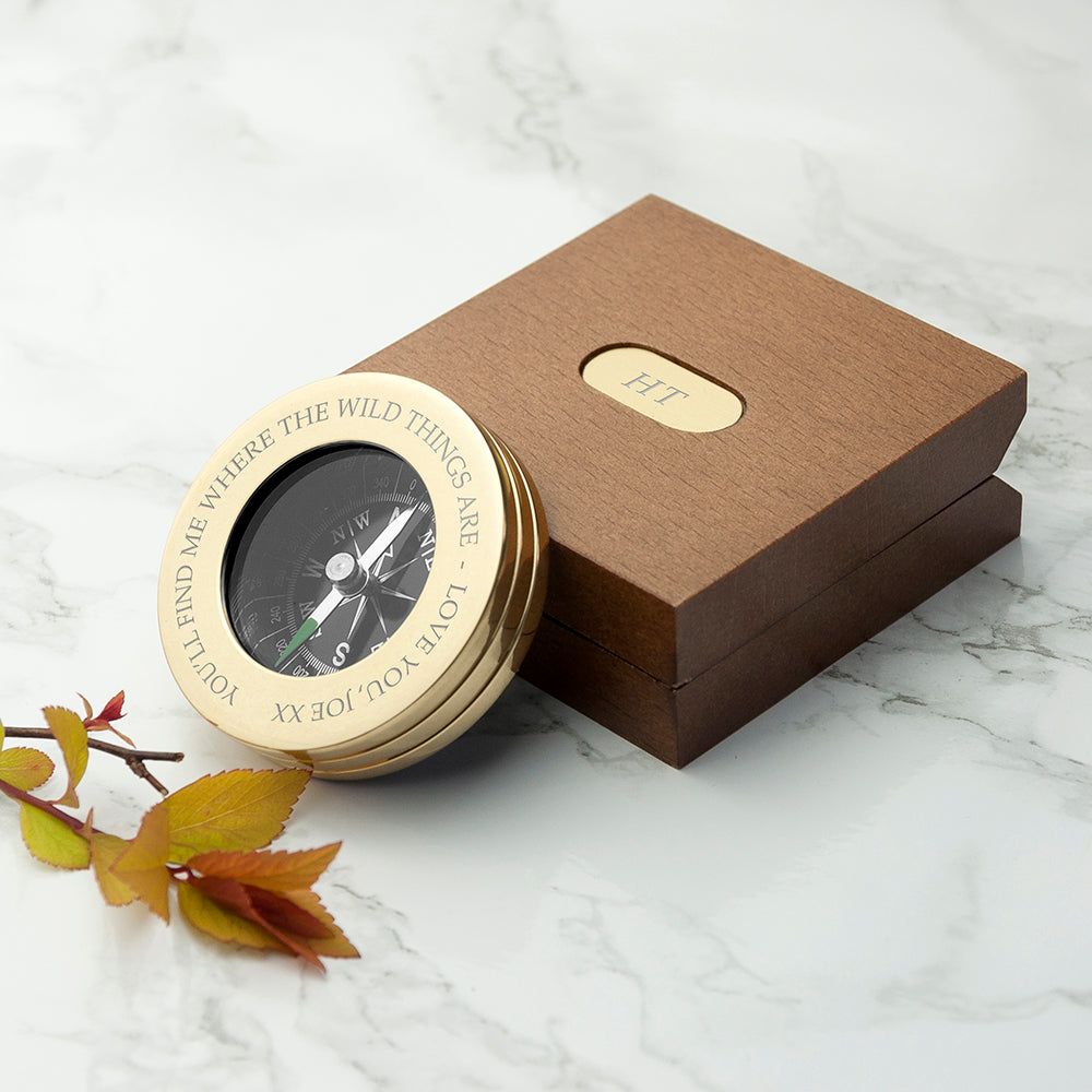Gold compass with engraved text on a brown box on a marble surface