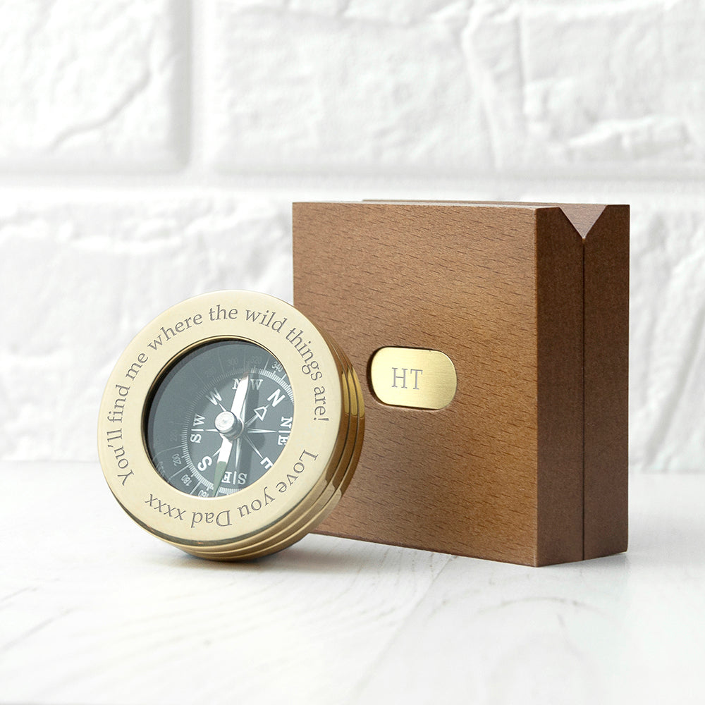 Gold compass with engraved text in a wooden box on a textured white background