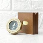 Gold compass with engraved text in a wooden box on a textured white background