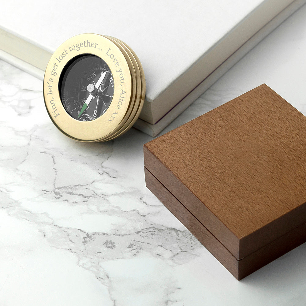 Gold compass with engraved text next to a wooden box on a marble surface