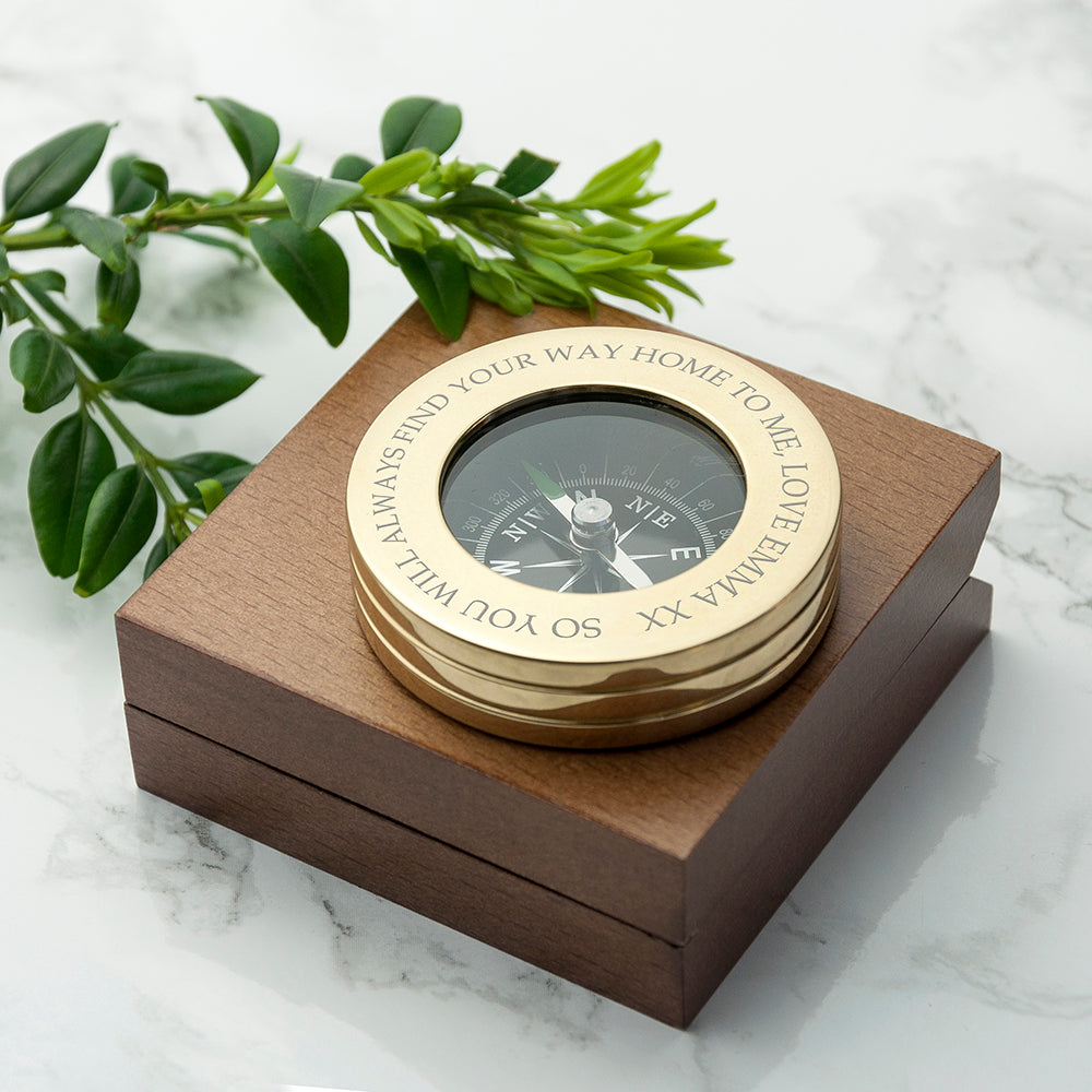 Gold compass in a wooden box on a marble surface with green leaves.
