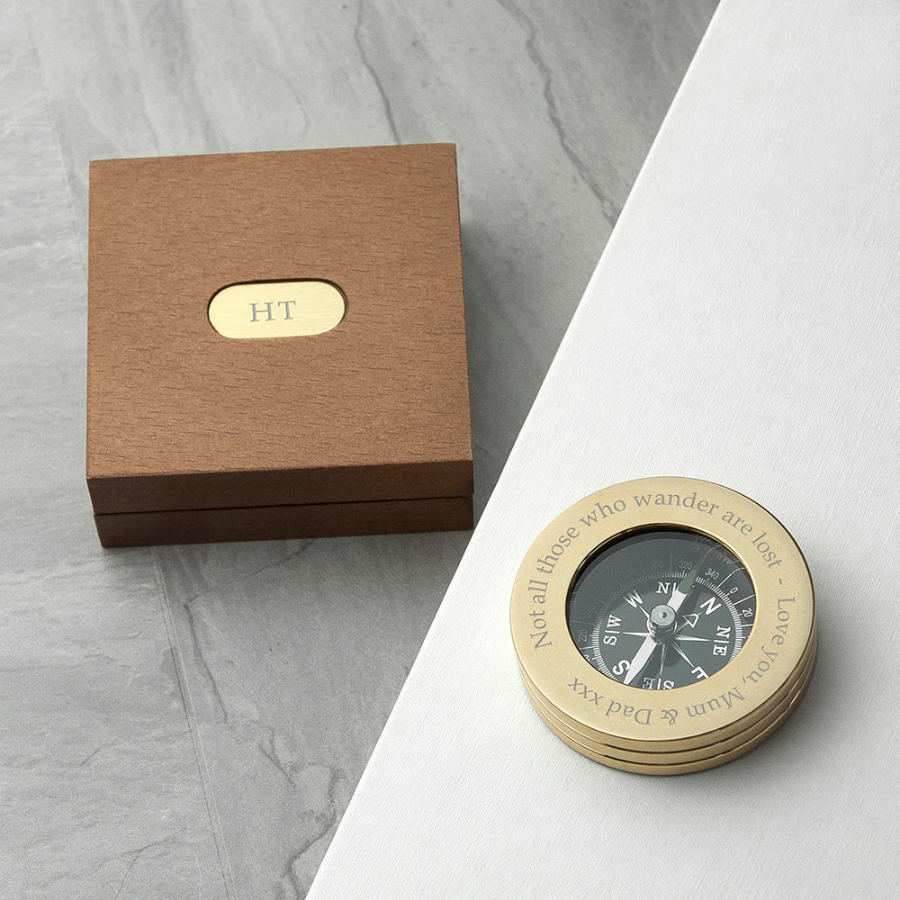 Gold compass with engraved text on a marble surface next to a brown box.