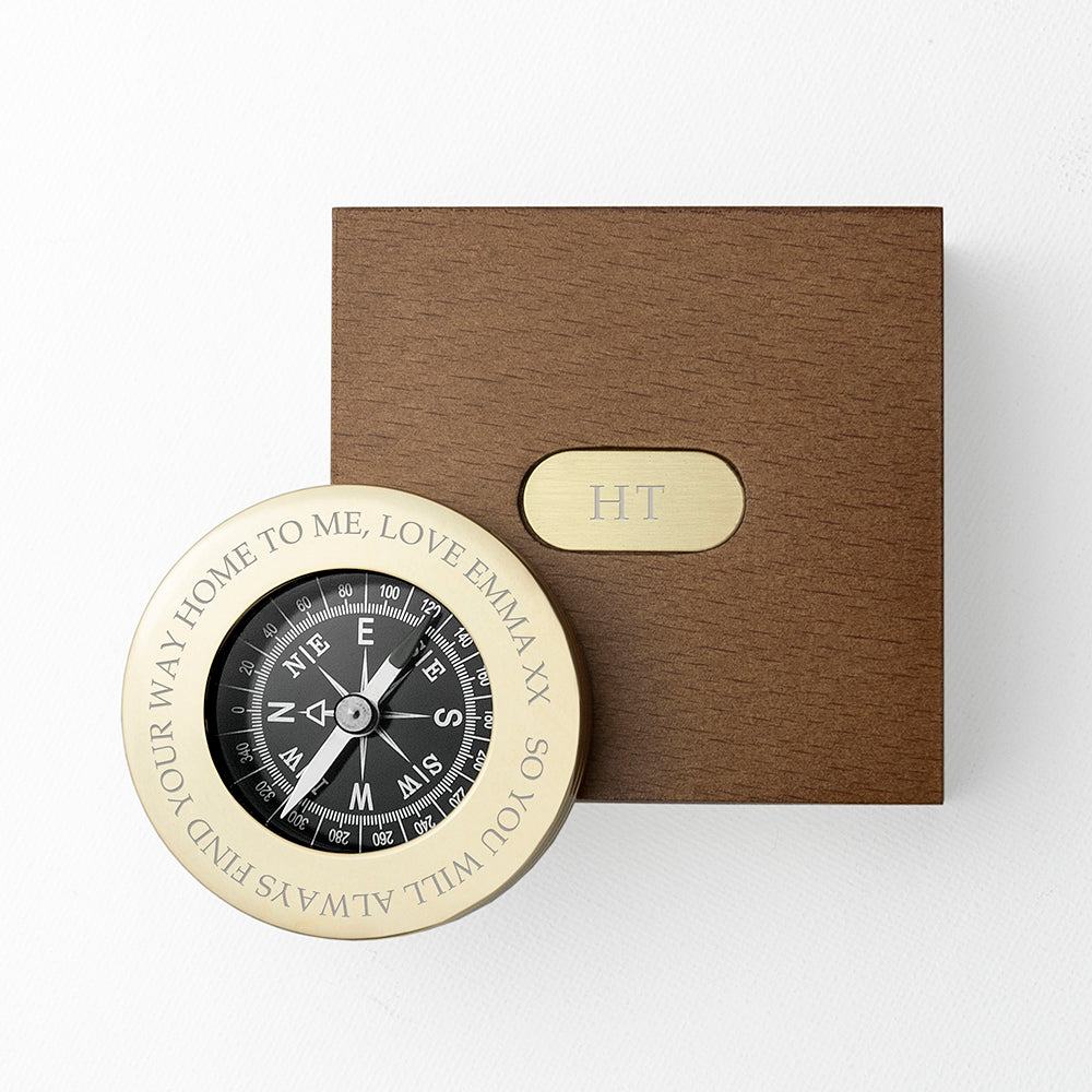 Brass compass with engraved text next to a brown box on a white background
