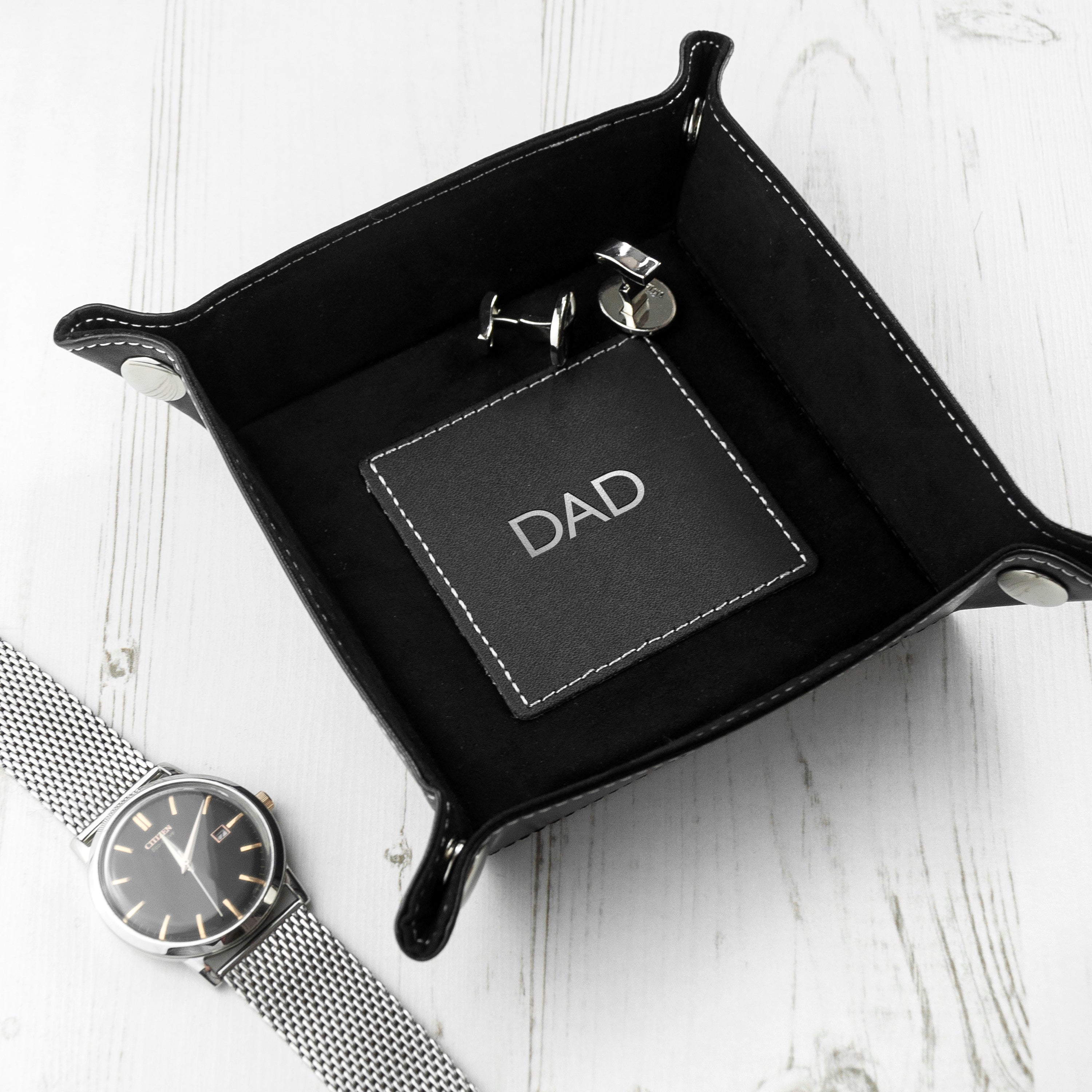 Black leather tray with 'CONNOR' branding, watch, and keychain on a white surface