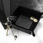 Black leather tray with car keys, wallet, and coins on a white surface