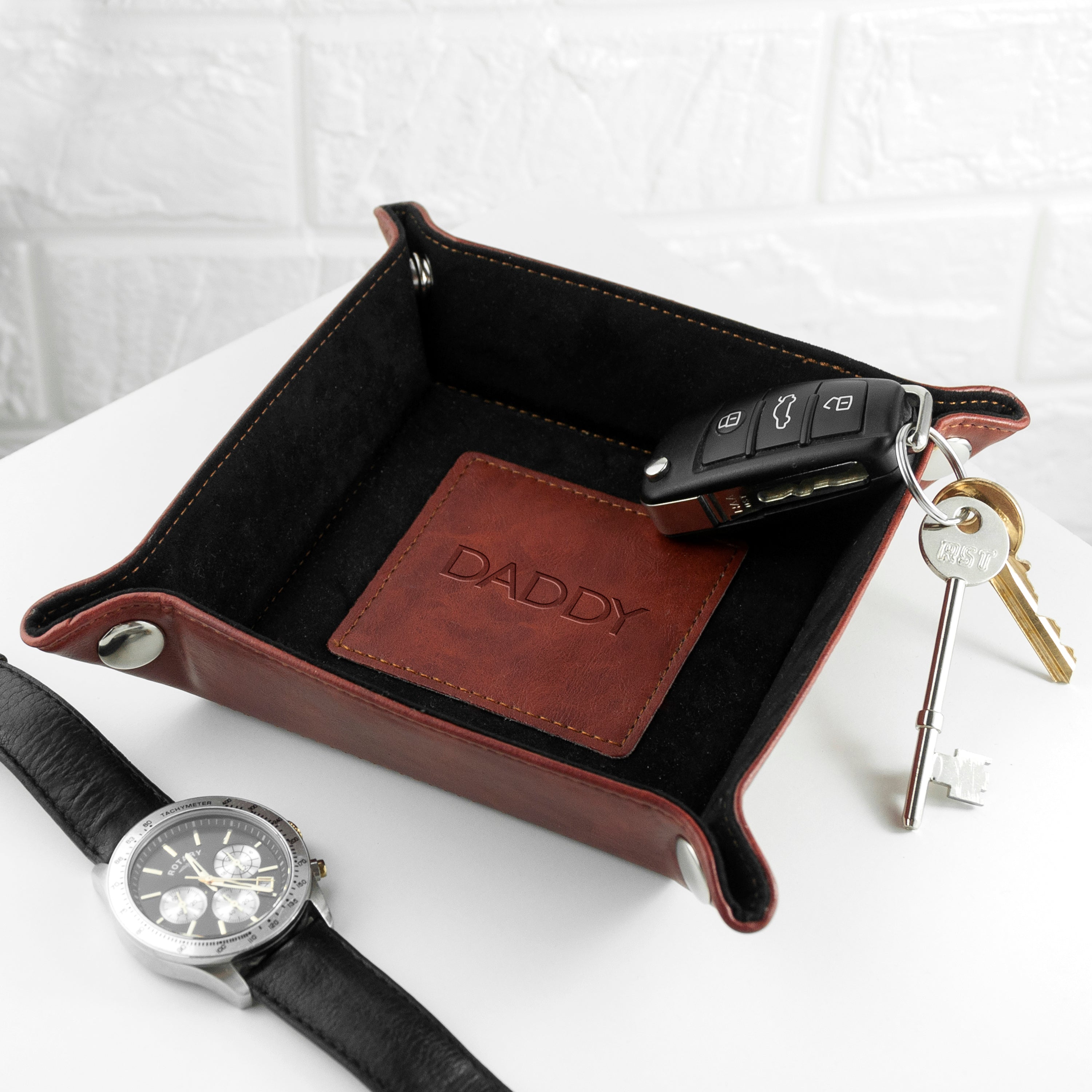 Black leather tray with 'DADDY' patch, car keys, and watch on a white background