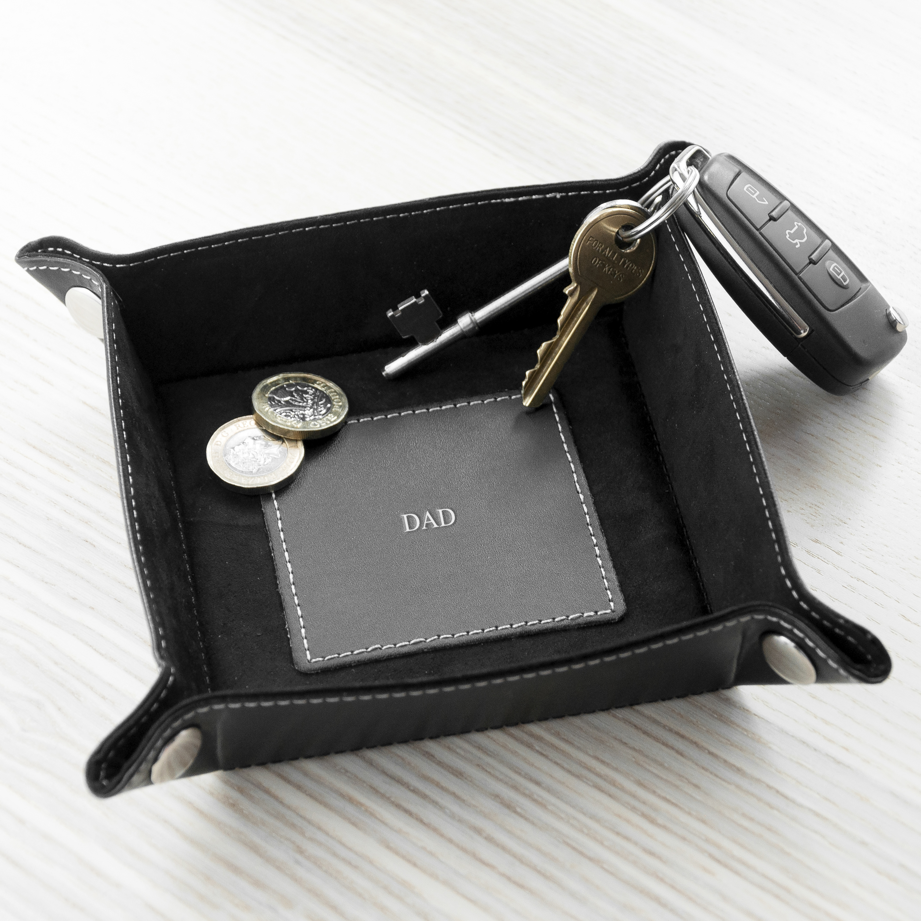 Black leather tray with keys, coins, and a card labeled 'DADDY' on a white surface.