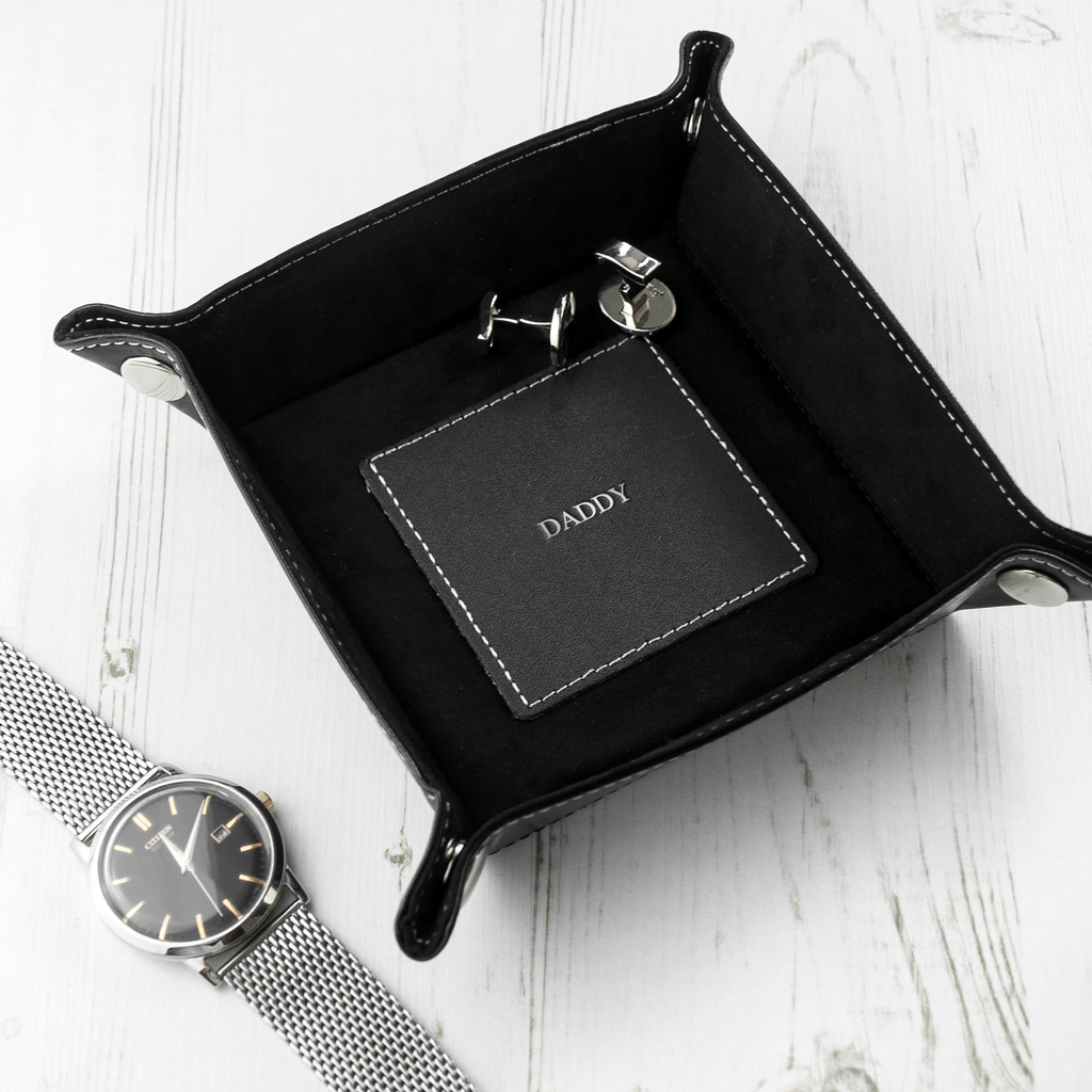 Black leather tray with 'CONNOR' branding, watch, and keychain on a white surface