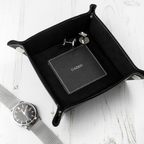 Black leather tray with 'CONNOR' branding, watch, and keychain on a white surface