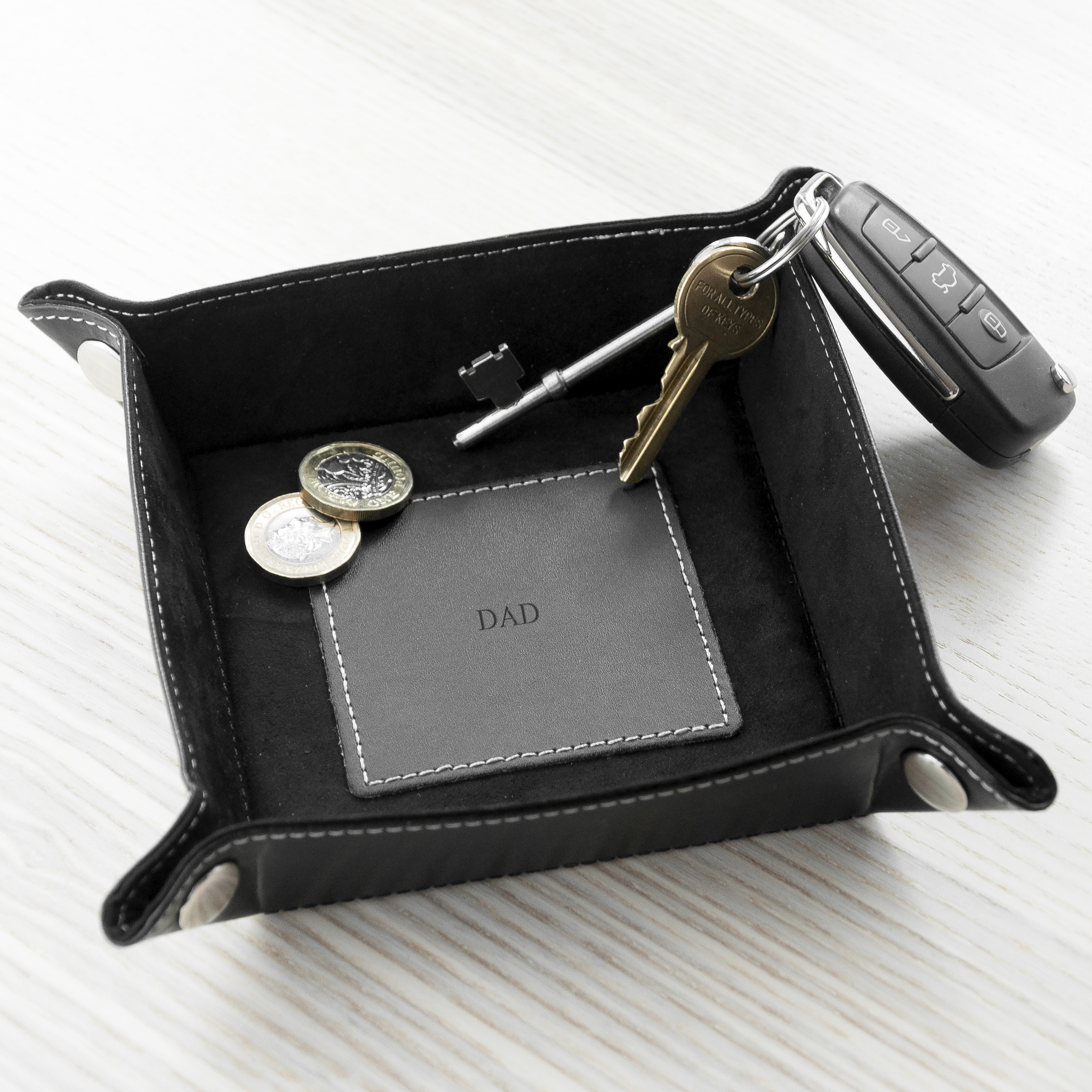 Black leather tray with 'DAD' card and keys on a white surface