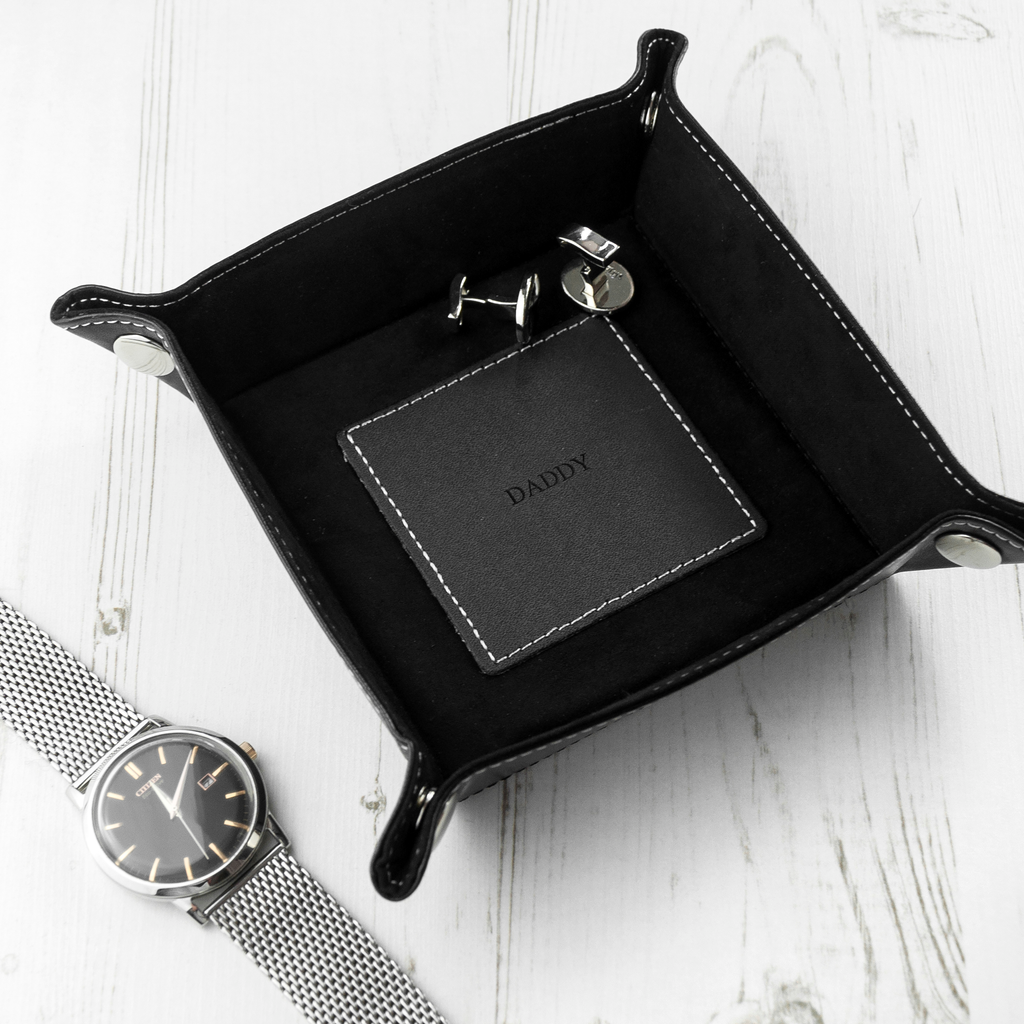 Black leather tray with 'CONNOR' branding, watch, and keychain on a white surface
