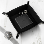 Black leather tray with 'CONNOR' branding, watch, and keychain on a white surface