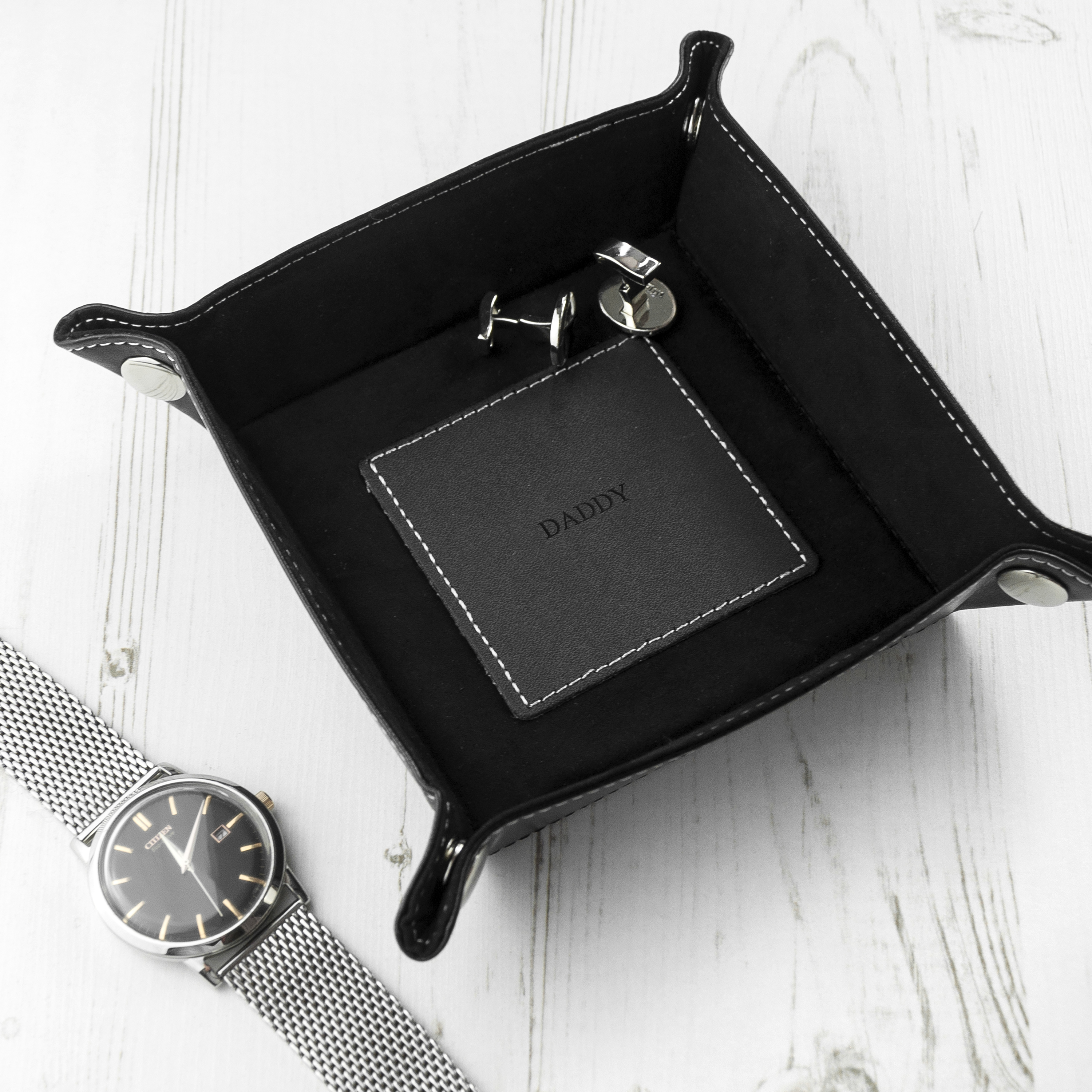 Black leather tray with 'CONNOR' branding, watch, and keychain on a white surface