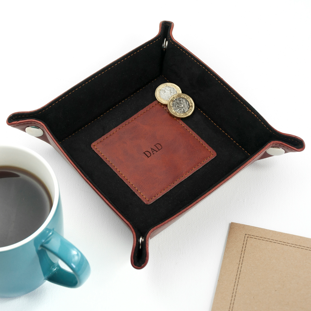 Black leather tray with 'DAD' engraving next to a blue mug and notebook on a white background