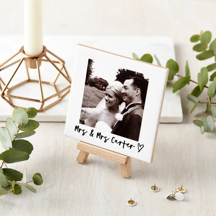 Small easel with a photo of a couple labeled 'Mrs & Mrs Carter' on a decorative surface with greenery.
