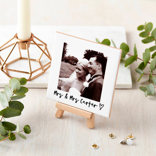 Small easel with a photo of a couple labeled 'Mrs & Mrs Carter' on a decorative surface with greenery.