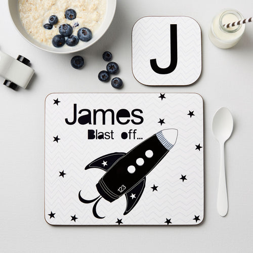 Placemat with a rocket design and 'James Blast off' text on a table with a bowl of cereal and blueberries.