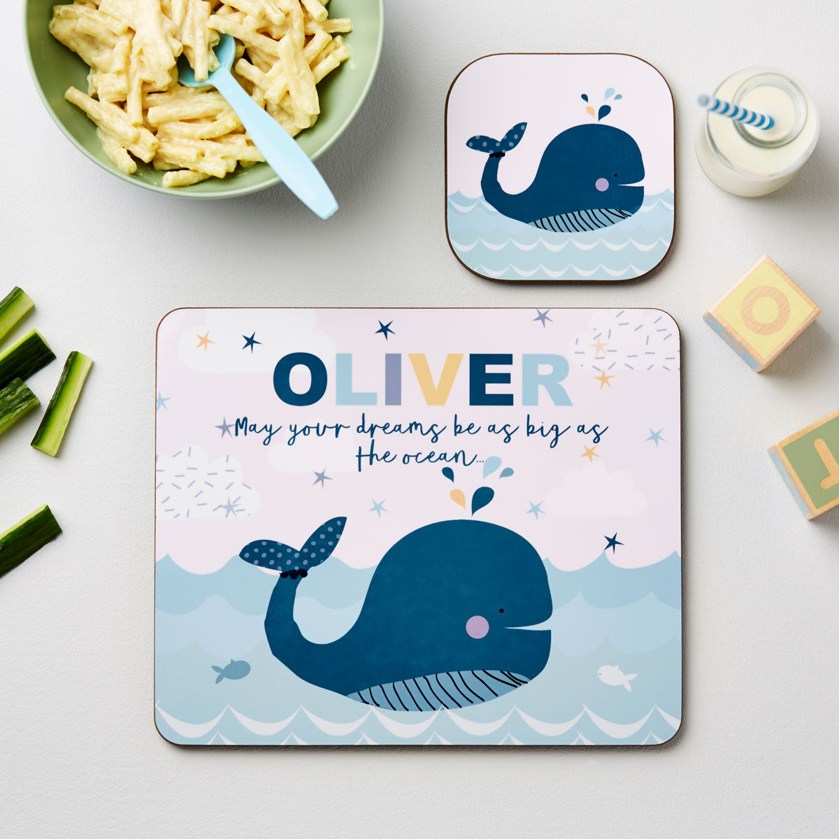 Two whale-themed placemats with 'OLIVER' and motivational quote on a table with food and blocks.