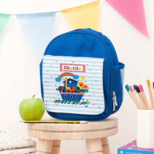 Blue children's lunch bag with a colorful design on a wooden stool with stationery items.