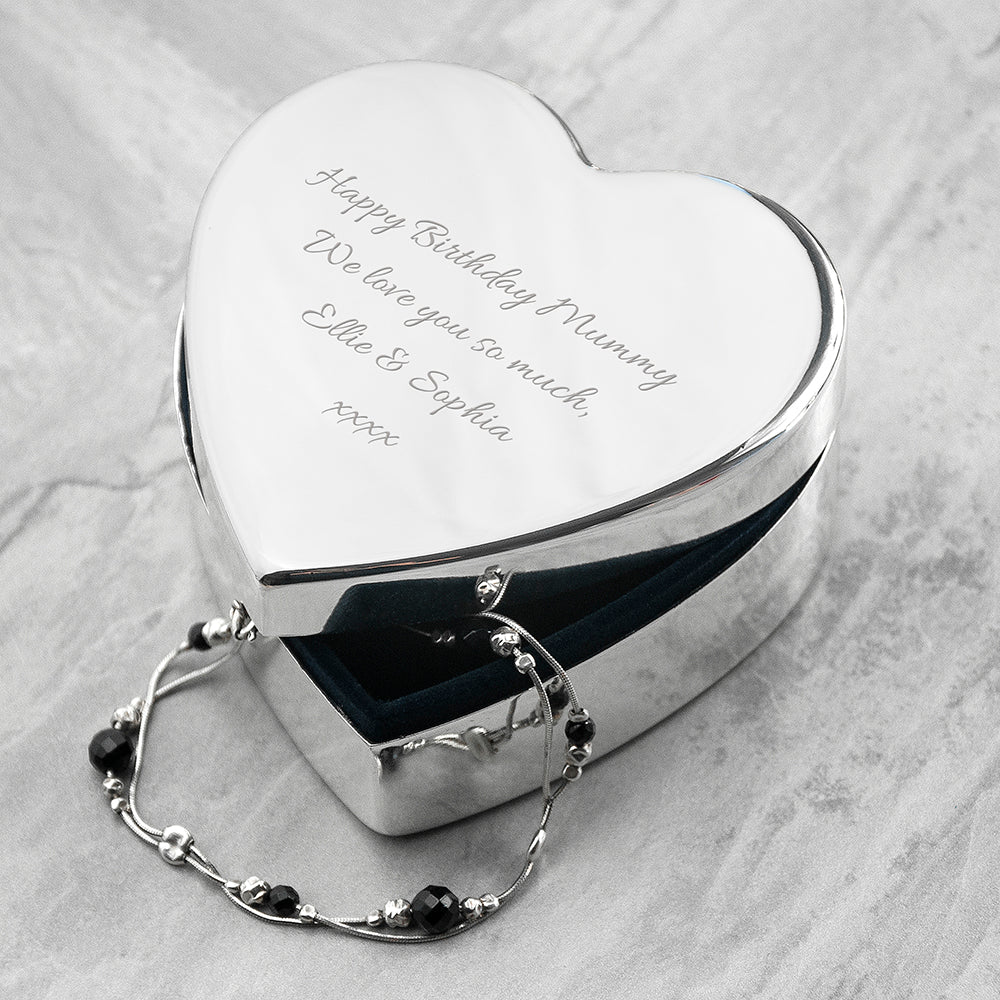Heart-shaped silver jewelry box with engraved message on a light gray surface