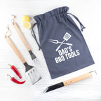 Gray drawstring bag with 'Dad's BBQ Tools' text, accompanied by barbecue utensils on a white background.