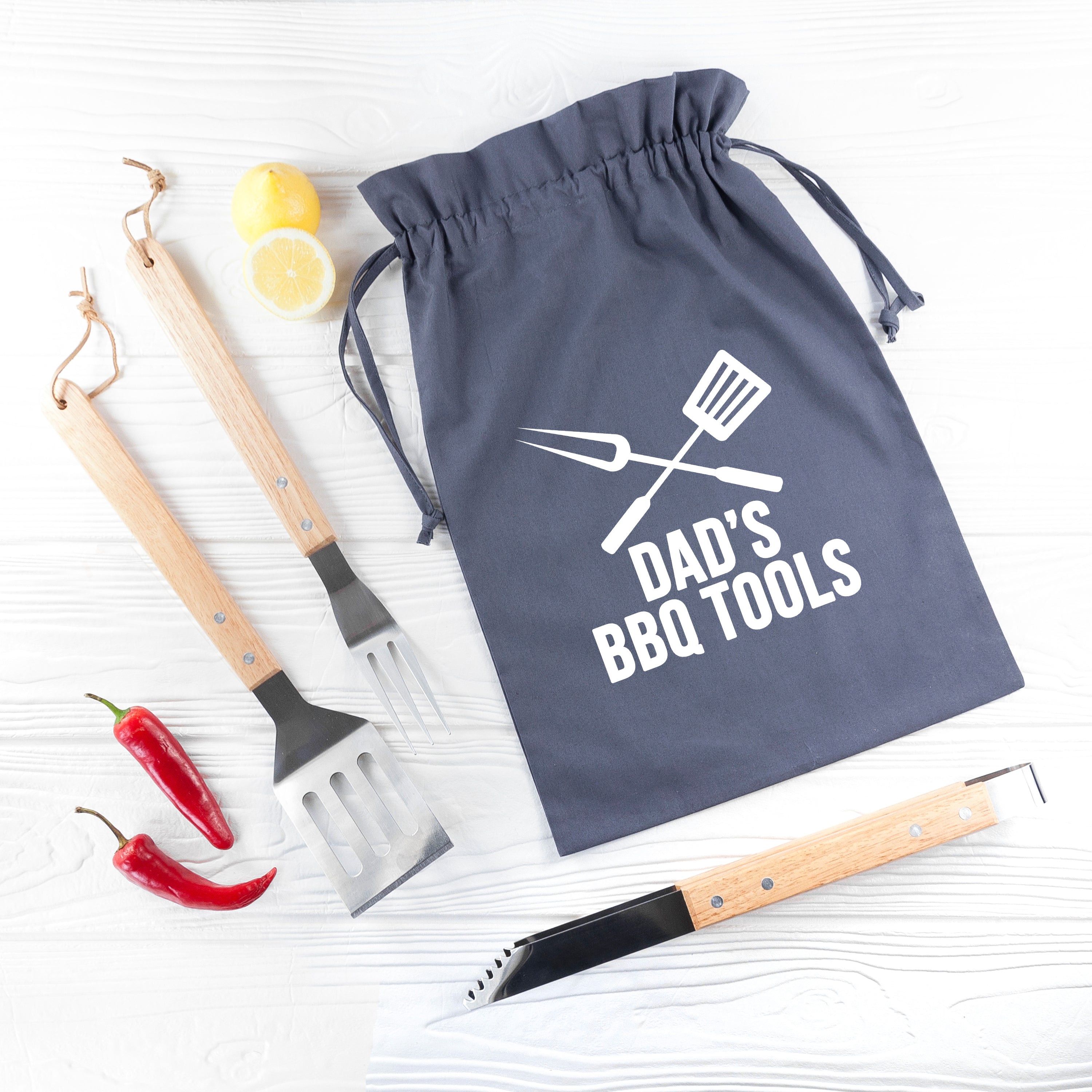 Gray drawstring bag with 'Dad's BBQ Tools' text, accompanied by barbecue utensils on a white background.