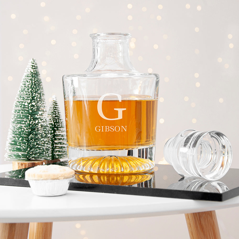 Clear glass decanter with 'G' and 'GIBSON' engraving on a table with a blurred Christmas tree in the background.