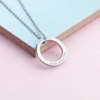 Silver ring-shaped pendant necklace on a pastel pink and blue background
