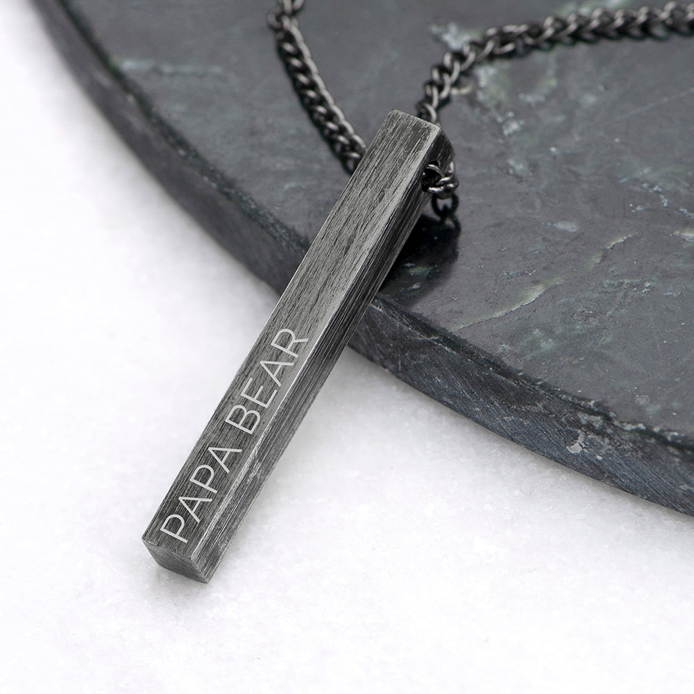 Necklace with a pendant engraved 'PAPA BEAR' on a dark surface.