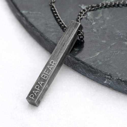 Necklace with a pendant engraved 'PAPA BEAR' on a dark surface.