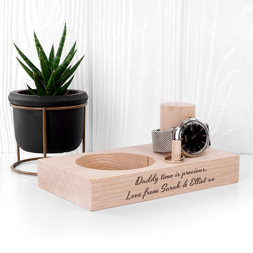 Wooden desk organizer with a watch, candle, and small plant on a white surface.