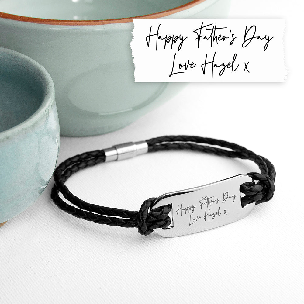 Black braided bracelet with engraved message on a white surface with ceramic bowls in the background.
