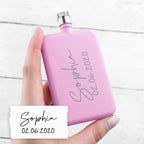 Hand holding a pink flask with engraved text on a white background