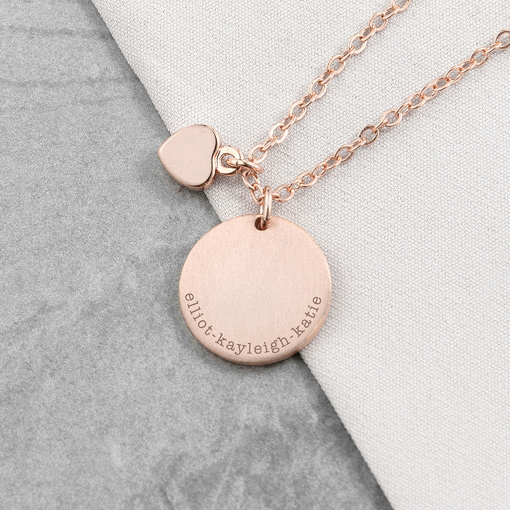 Rose gold necklace with a round pendant and heart charm on a gray and white background