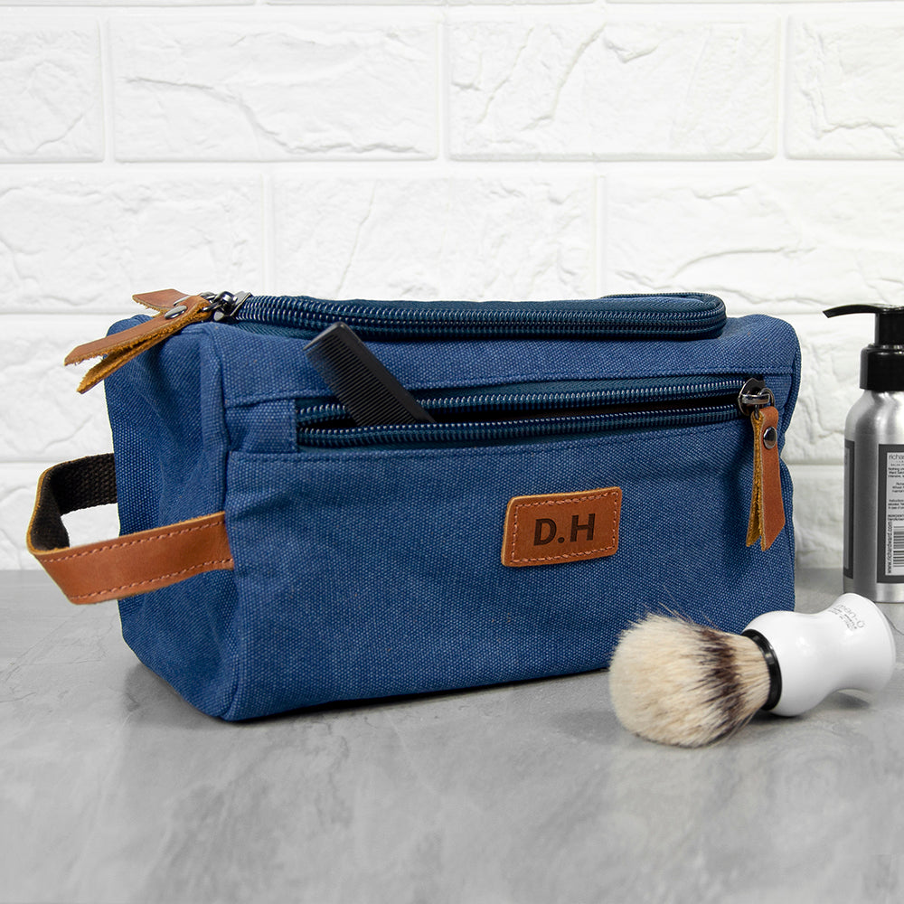 Blue toiletry bag with brown leather accents on a textured surface