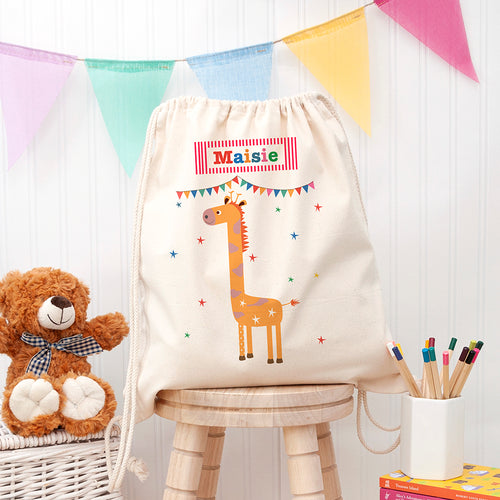 Children's drawstring bag with a giraffe design and 'Maisie' text, placed on a wooden stool with a teddy bear and books in the background.